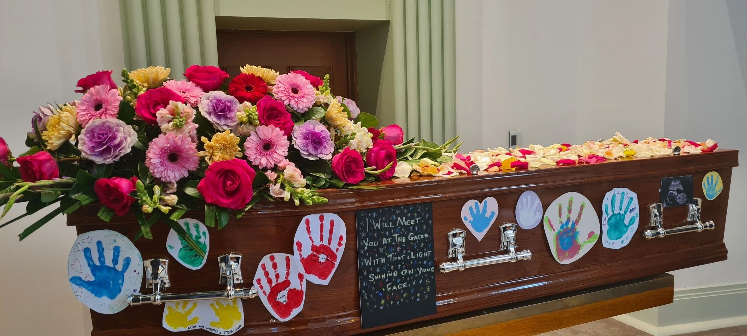 A decorated coffin with colorful flowers and children's handprint notes.