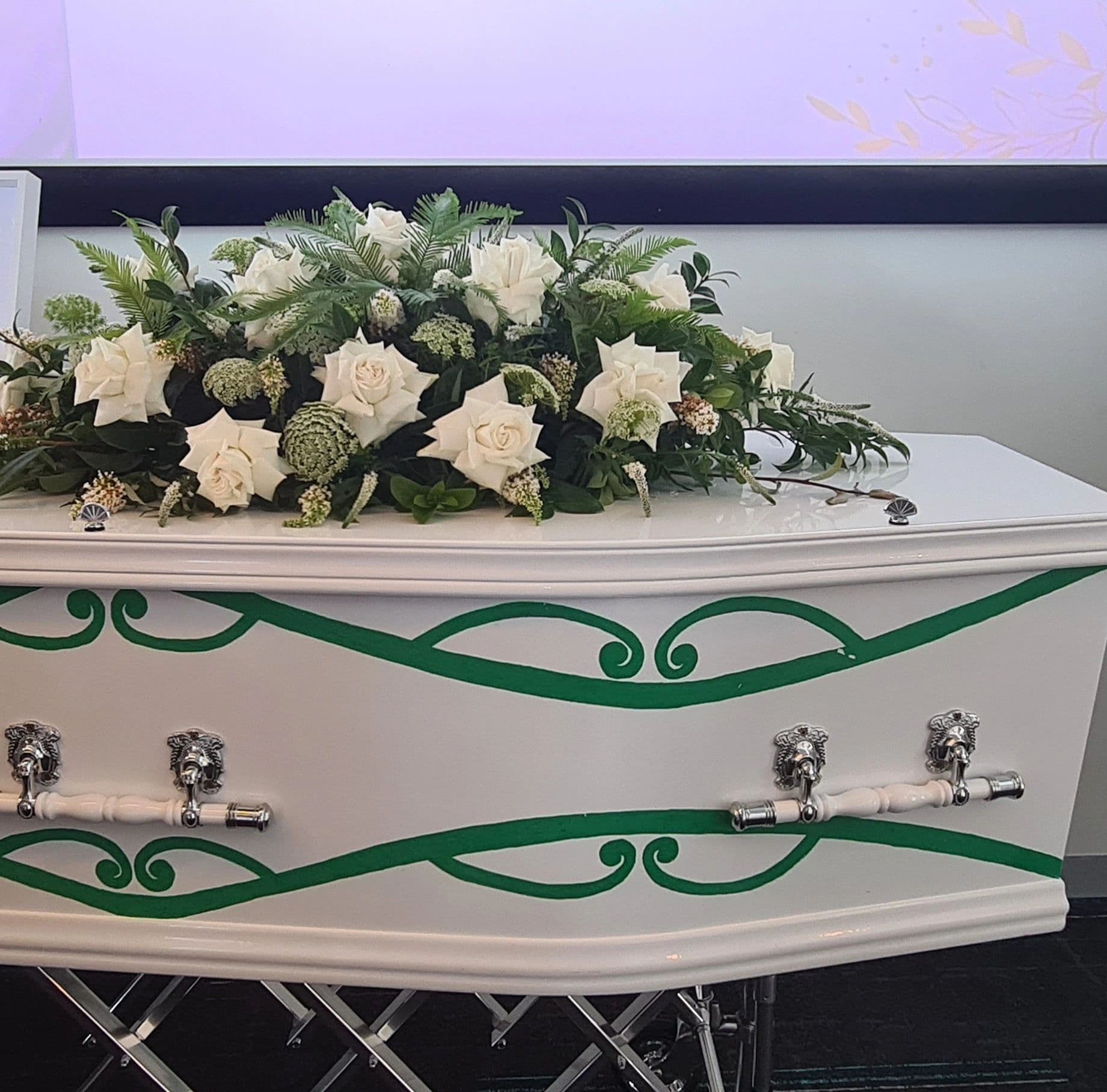 White coffin adorned with white roses and green leaves.