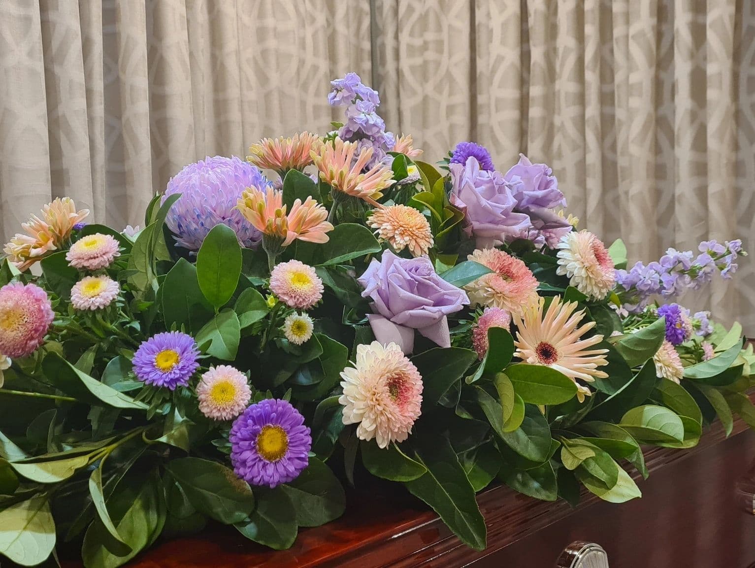 A colorful floral arrangement with purple, pink, and peach flowers and lush green leaves.