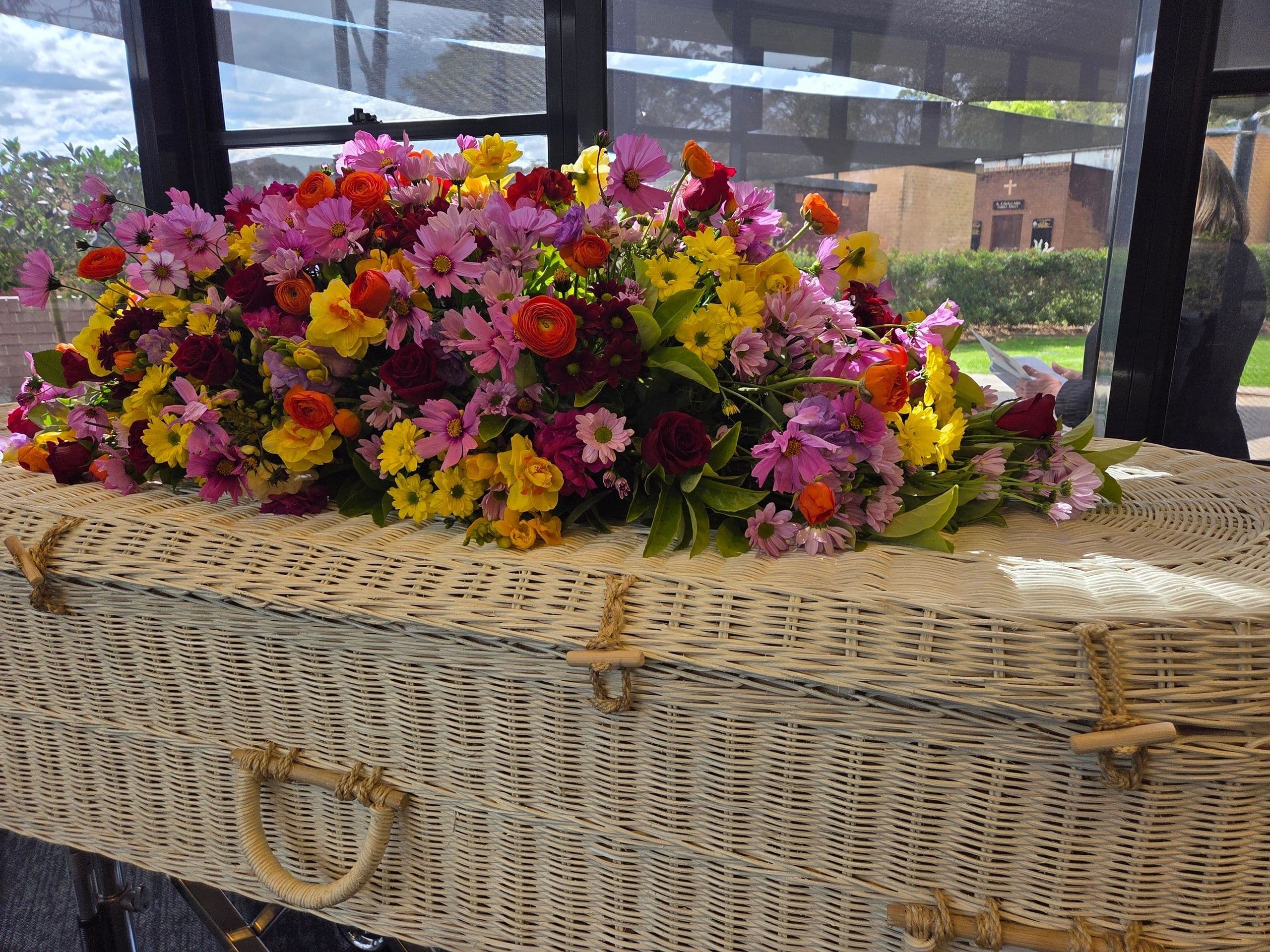 Wicker coffin adorned with colorful flowers at a funeral service.