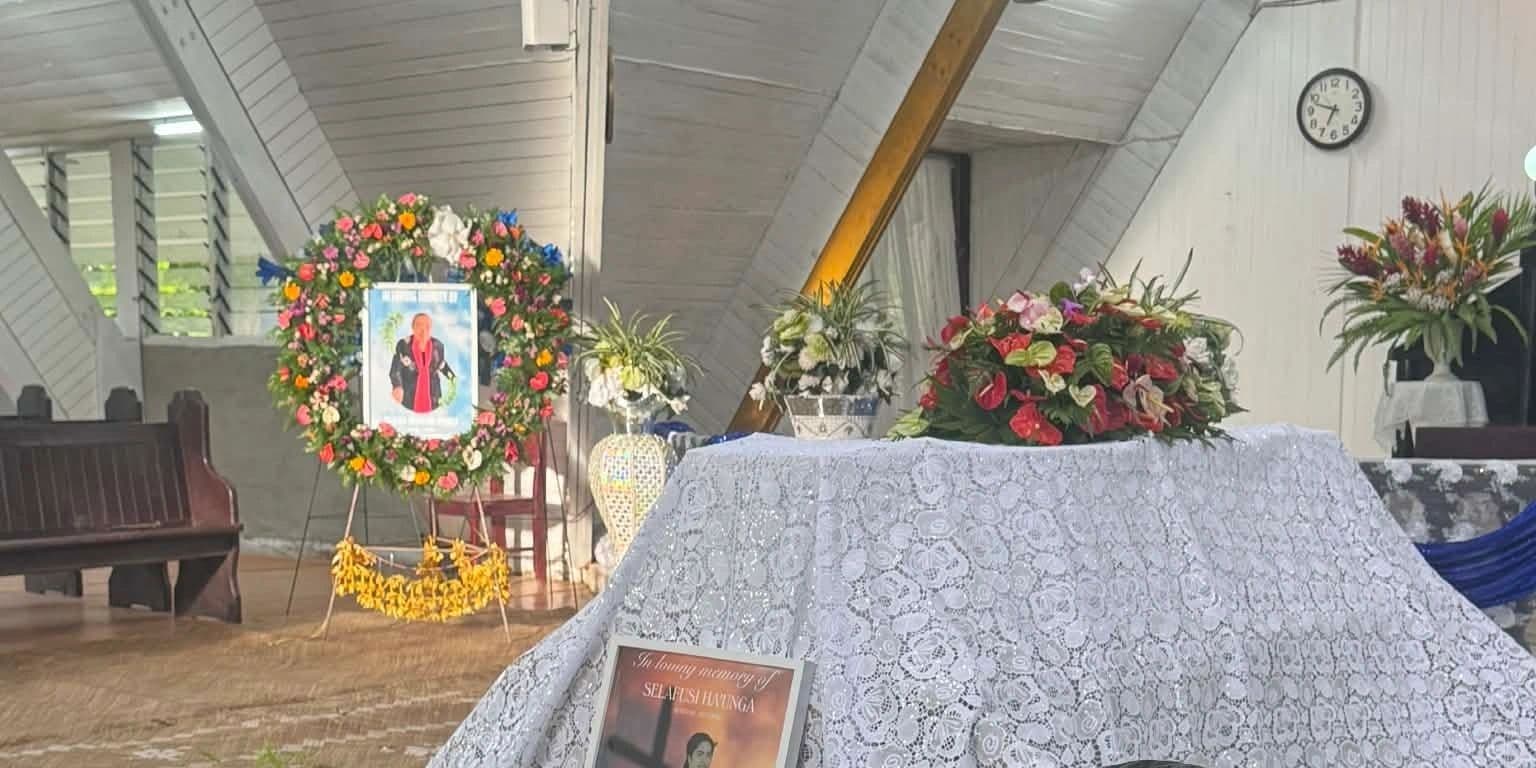 A floral-decorated memorial setup inside a chapel with a photo and a book on a lace-covered table.