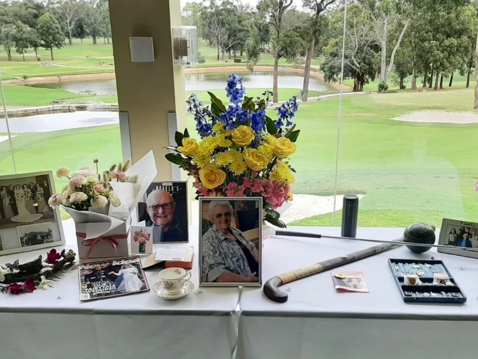 Memorial table with photos, flowers, and personal items overlooking a golf course.