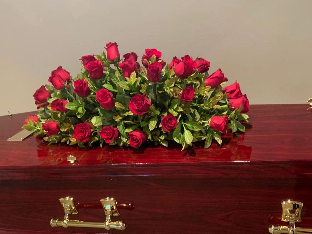 A bouquet of red roses on a polished wooden coffin.
