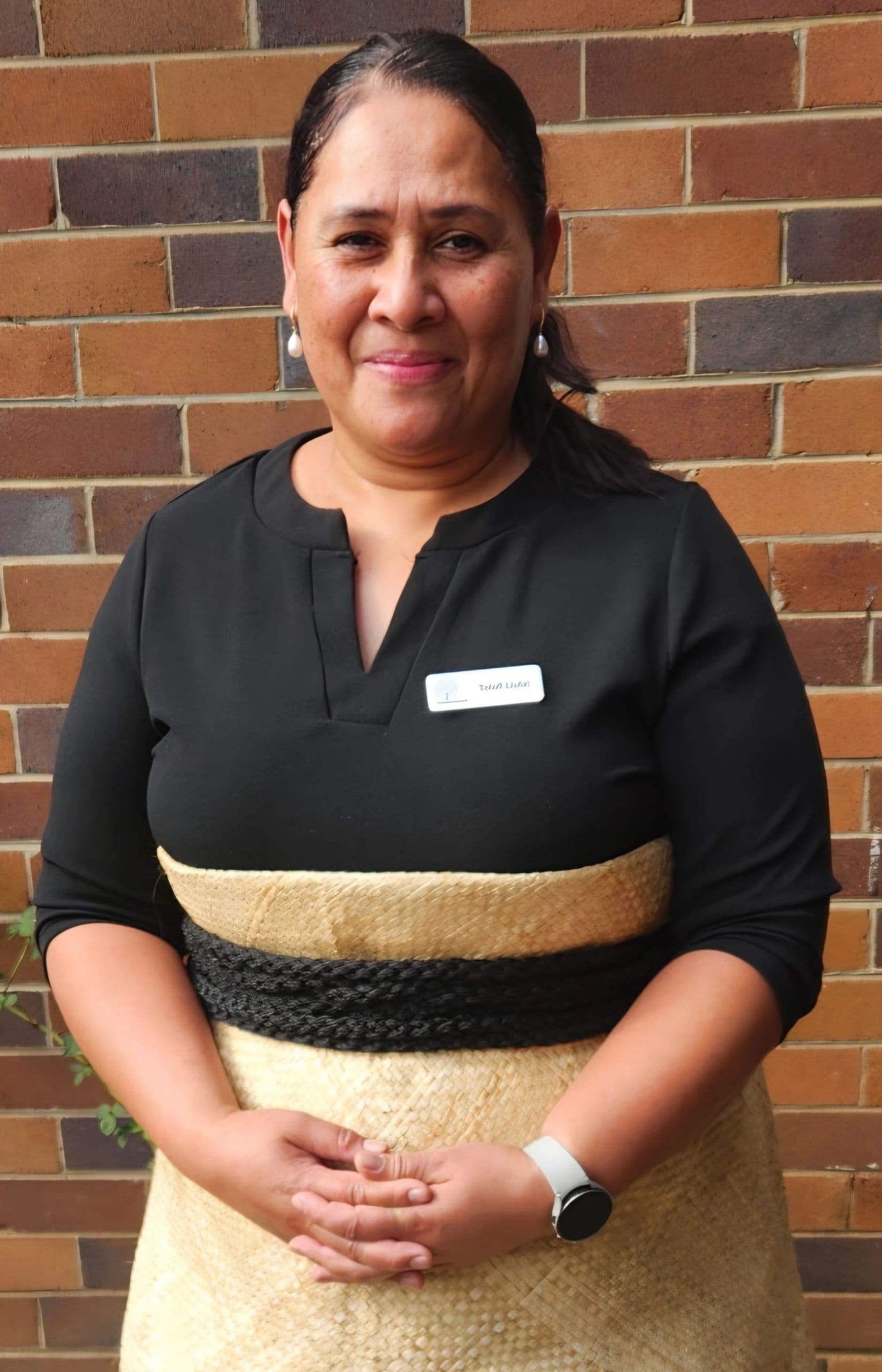 Woman in traditional attire standing against a brick wall, smiling.