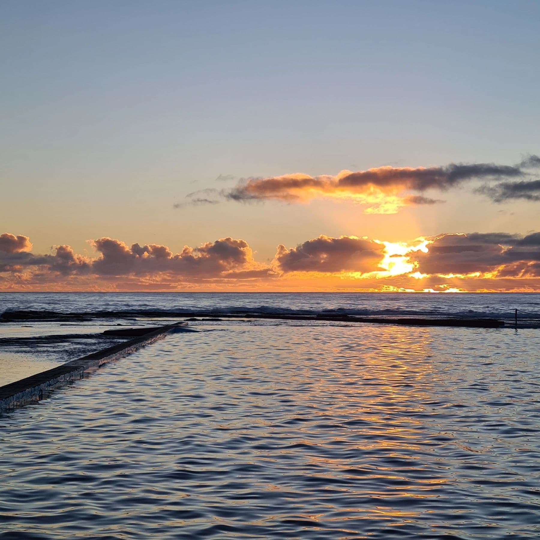 Sunset over a calm ocean pool with scattered clouds.