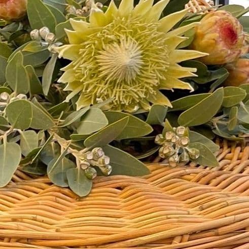 A close-up of a yellow flower with green leaves on a woven basket.