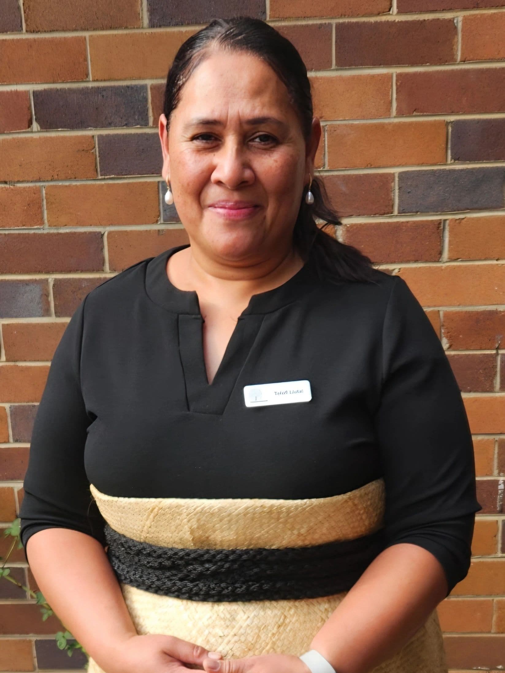 Woman in traditional attire standing against a brick wall, smiling warmly.